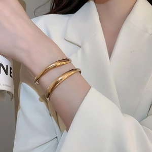 Polished gold geometric double-layered open cuff bracelets on model wrist with white blazer