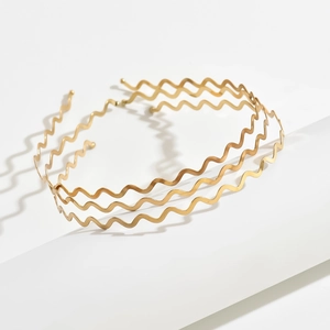 Three minimalist gold wave metal headbands displayed on white minimalist props