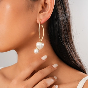 Gros plan de boucles d'oreilles dorées avec perles cœur et rondes sur un mannequin