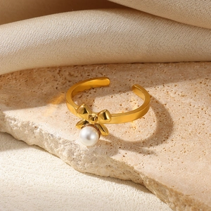 Detailed shot of a gold bow ring with a white pearl on elegant champagne silk fabric