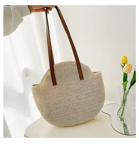 Detail of straw woven tote bag featuring beige texture and brown leather shoulder straps