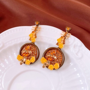 Macro shot of vintage floral lute-shaped earrings with orange crystals on white porcelain