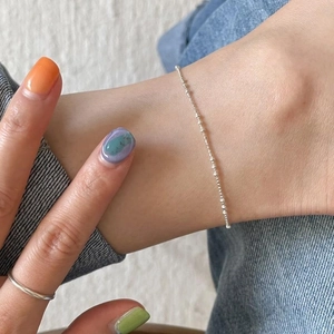 Close-up of a delicate 925 sterling silver beaded anklet on a woman's ankle