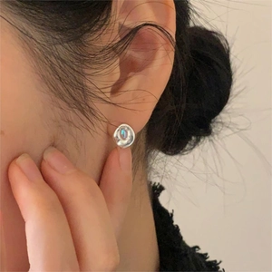 Close-up of minimalist 925 silver stud earrings with iridescent blue gemstones on an ear
