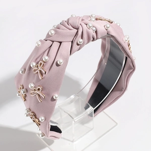 Detailed view of pink knotted headband with white pearls and gold-rimmed bow accents