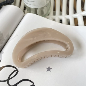 Close-up of a glossy beige crescent hair claw clip resting on a white art book