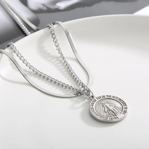 Macro shot of silver layered necklace with Virgin Mary pendant and flat snake chain