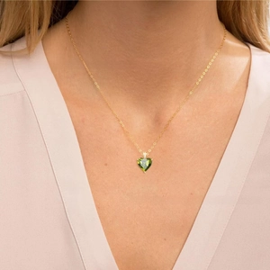 Modell trägt goldene Herzanhängerkette mit grünem Peridot-Stein und feinem Zirkon-Besatz