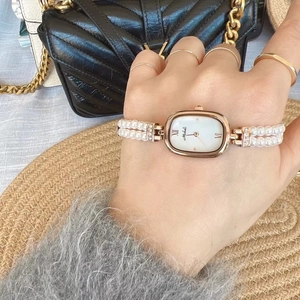 Elegante goldene Oval-Uhr mit Perlenarmband auf einer luxuriösen Handtasche