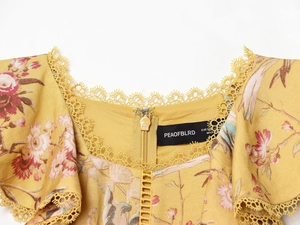 Dettaglio dello scollo all'americana in pizzo con stampa floreale rosa su tessuto giallo