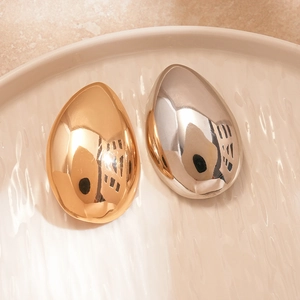 Polished gold and silver metallic droplet pins displayed on a textured ceramic plate