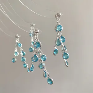 Macro detail of silver tassel earrings featuring blue resin stones and dangling chains
