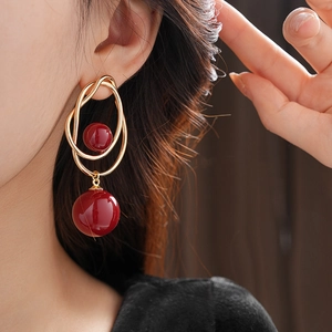 Detail of gold geometric double hoop earrings with deep red resin pearls on model