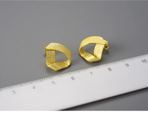 Detailed view of gold twisted ribbon earrings with brushed texture against a metric ruler