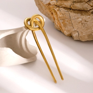 Detail of 18k gold plated stainless steel knot hair fork on a white ceramic plate