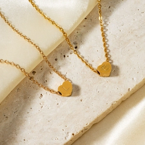 Elegant gold heart pendant necklaces with engraved letters on silk and stone background