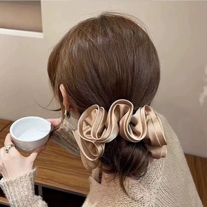 Detail of a large champagne silk satin scrunchie worn on a low bun hairstyle