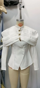 Detail of white tailored blazer featuring sculptural gold buttons and layered lapel design