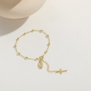 Minimalist 14K gold plated cross and holy medal bead bracelet for women on textured background