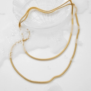 Minimalist double layer gold snake chain necklace displayed on a textured glass tray