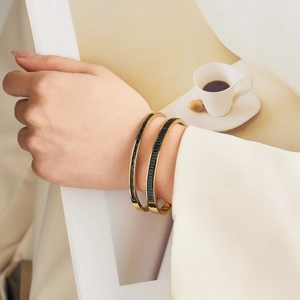 Detail of stacked gold-plated stainless steel bracelets with black emerald-cut crystals