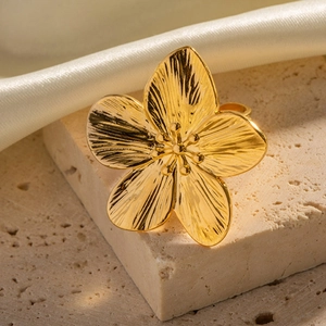 Exaggerated golden flower ring in stainless steel on textured stone with silk backdrop