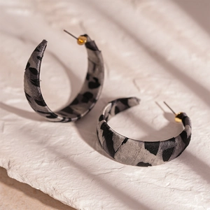 Detailed close-up of leopard print fabric-wrapped C-shape earrings on a white stone tray