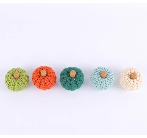 Row of five colorful knitted pumpkins in green, orange, blue, and beige for party decor