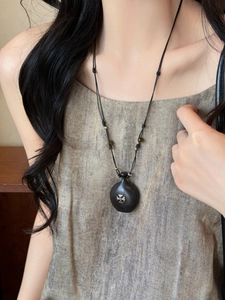 Close-up of ebony wood gourd pendant with silver cross inlay on black woven cord