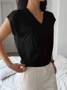 Close-up of black V-neck knit vest featuring large 3D floral decoration and ribbed hem
