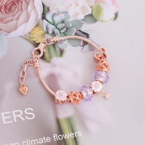 Rose gold charm bracelet with purple beads and pink cherry blossom pendants in floral setting