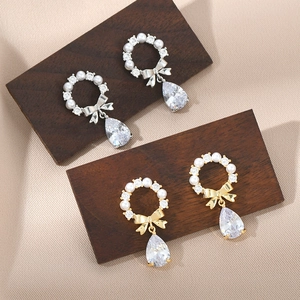 Close-up of pearl bow drop earrings in gold and silver finish with crystal zircon