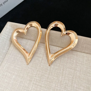 Detailed view of large gold heart hoop earrings with a polished mirror finish on beige fabric
