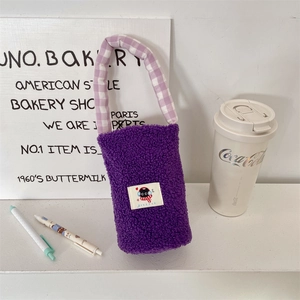 Detalle de bolsa de felpa morada para botella con asa de cuadros y parche de gato