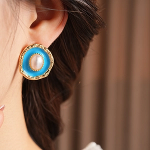 Close-up of vintage oval pearl earrings with sky blue enamel and golden metal texture