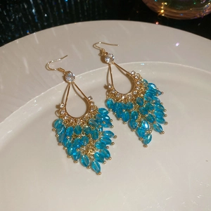 Detail view of gold teardrop earrings with crystals and blue glass bead tassels