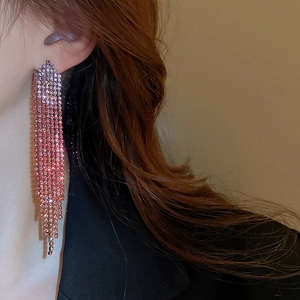 Detailed view of long pink gradient tassel earrings with rhinestones worn by a model