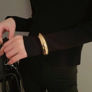 Polished wide gold bangle on a black knit sleeve showcasing a thick minimalist metal cuff