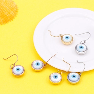 Detail of blue evil eye pearl earrings in gold and silver finish on a yellow background