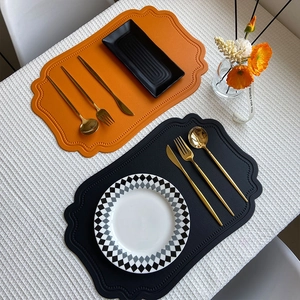Faux leather placemats in orange and black with scalloped edges on a textured cloth