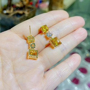 Détail de boucles d'oreilles dorées avec pierres jaunes carrées et strass blanc