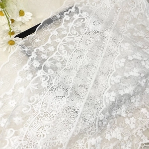 Close-up of white floral lace fabric with intricate embroidery and scalloped edges