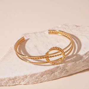 Macro detail of golden multilayer geometric open bangle with twisted wire and metal ring