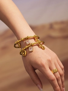 Detail of gold bracelets with zircon pendant and textured ring on model hand