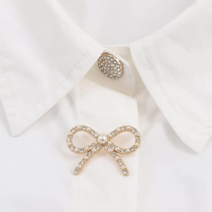 Detail of a golden bow brooch with white pearls and rhinestones on a poplin shirt collar