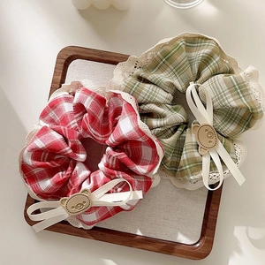 Close-up of bear-themed lace scrunchies in red and green checkered patterns with ribbons
