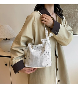 Detail of white fabric shoulder bag featuring black polka dots and a lace bow accent