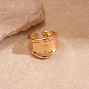 Detail of a wide gold-tone ring with irregular hammered texture on a stone surface