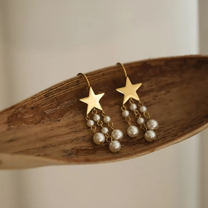 Macro shot of gold star earrings with pearl tassels on a textured bark background
