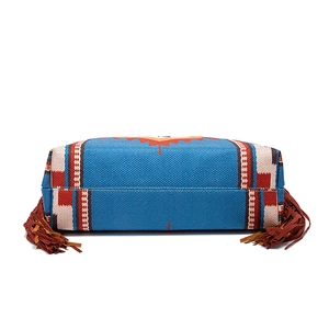 Macro shot of ethnic pattern woven fabric and brown fringe detail on blue shoulder bag